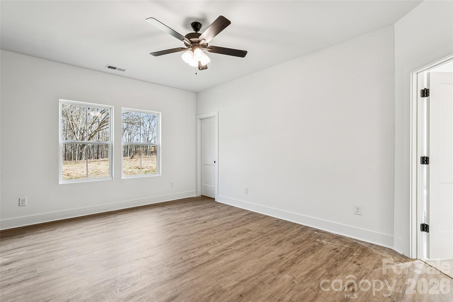 Second guest bedroom with ceiling fan, windows overlooking the backyard trees, and closet door