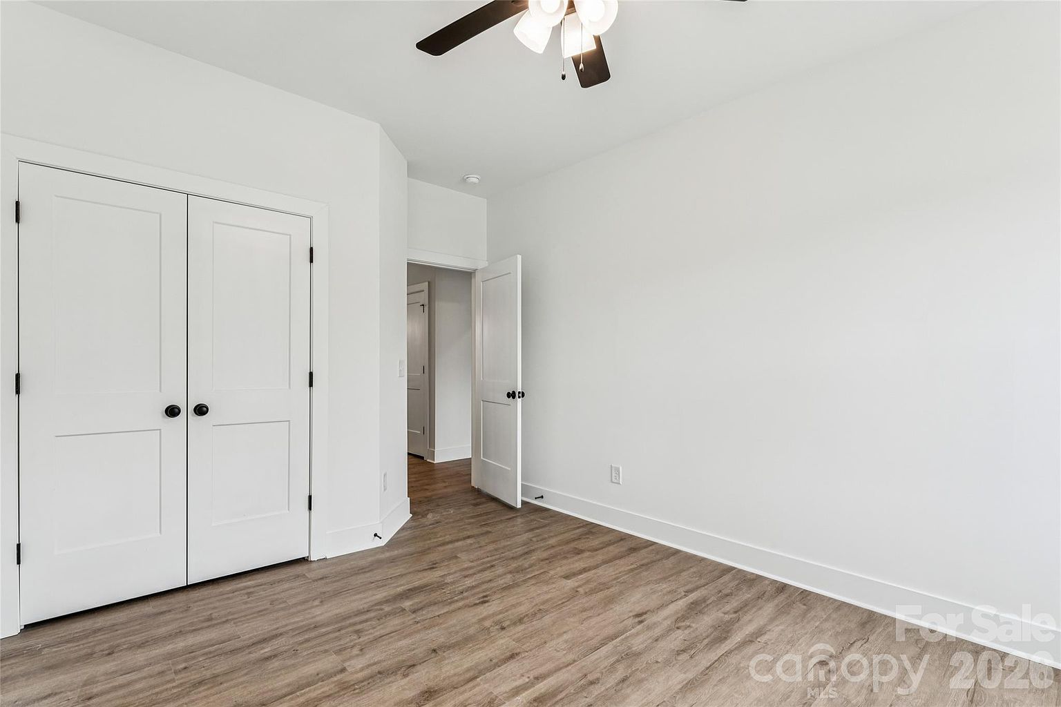 Bedroom with double closet doors, ceiling fan, and doorway to the hallway