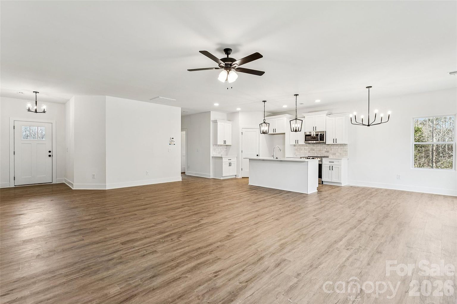 Open-plan great room and kitchen with hardwood-style floors, pendant lighting over the island, and front entry door visible to the left