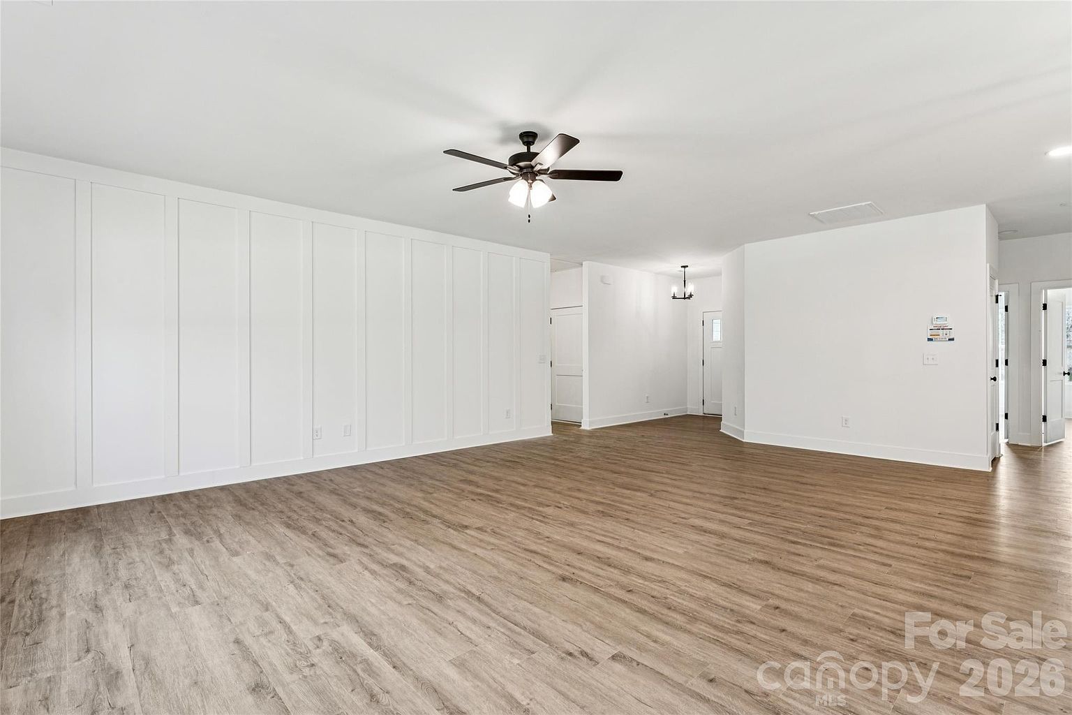 Great room with decorative board-and-batten accent wall, ceiling fan, and wide hallway leading to the bedrooms