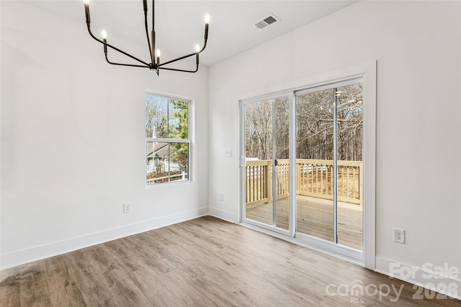 Dining space with modern chandelier, sliding glass door to the wooden deck, and a window looking out to trees
