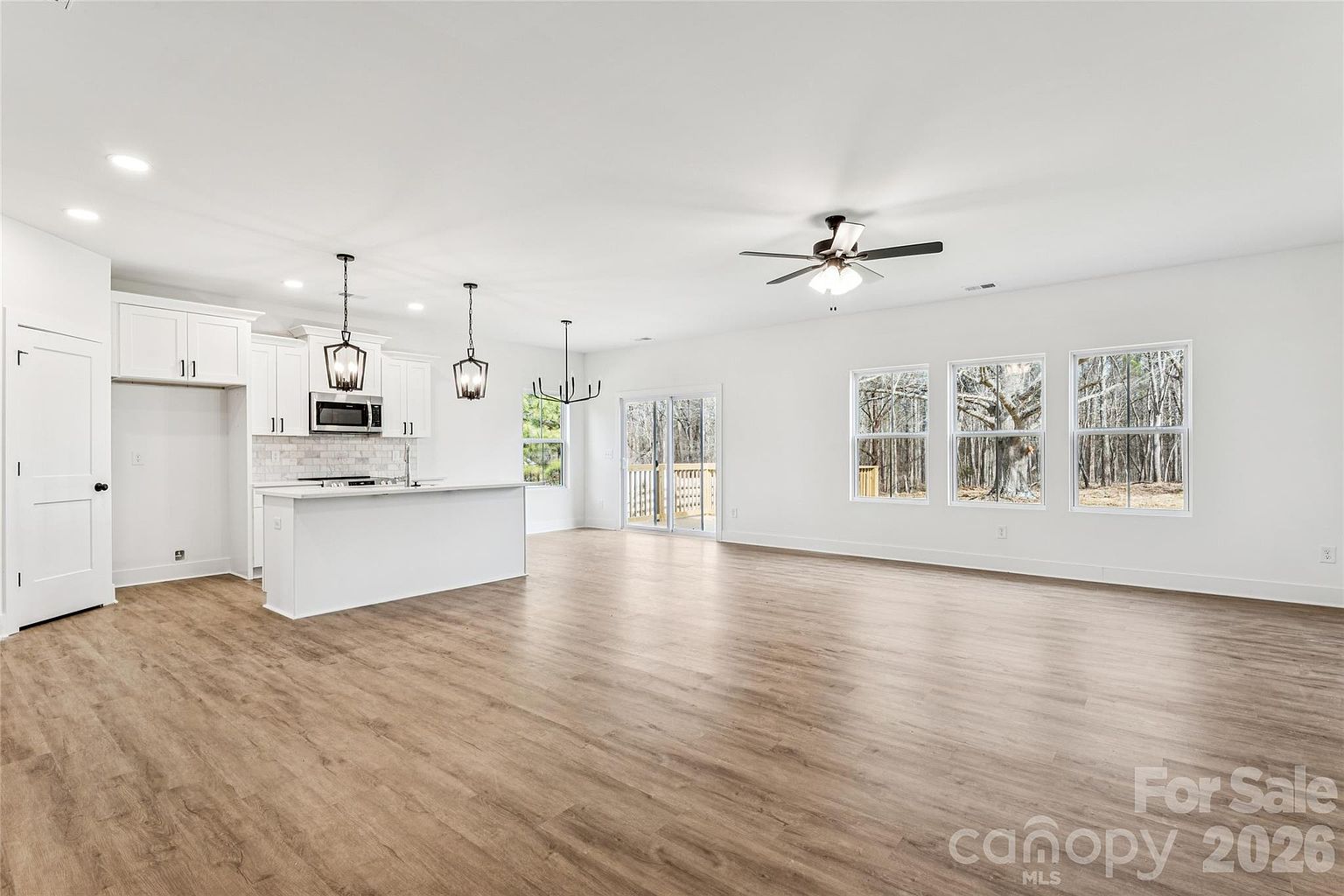 Panoramic view of the open living and kitchen area with large windows facing the wooded backyard