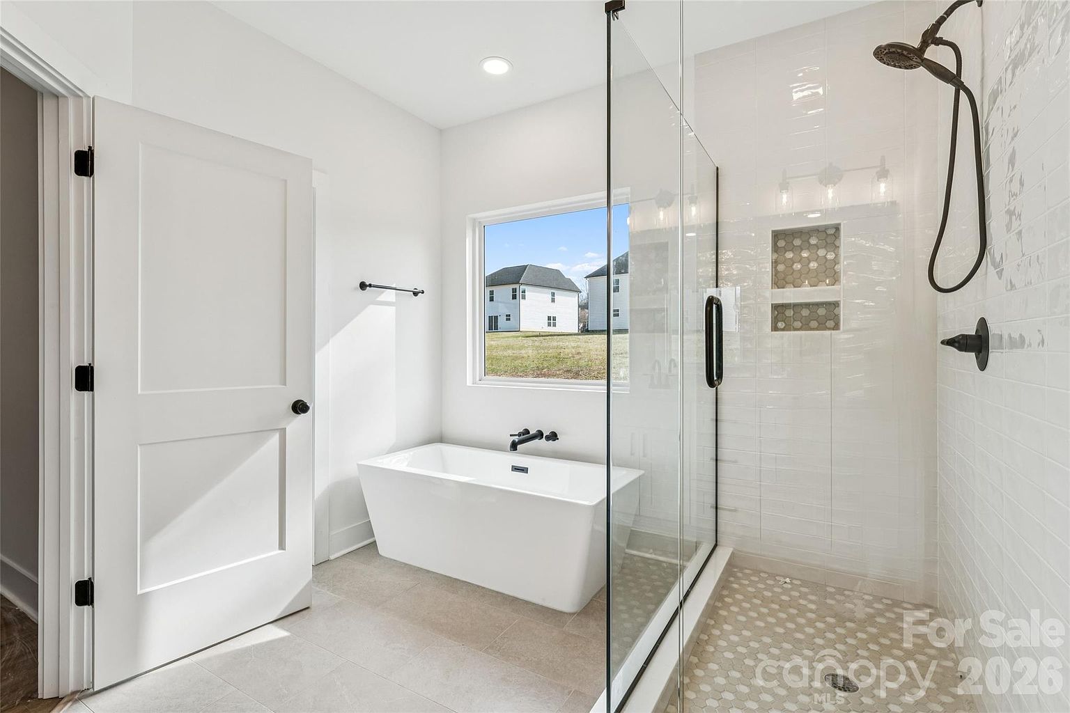 Primary bathroom with freestanding soaking tub, walk-in glass shower with tile accent niche, and natural light from a large window