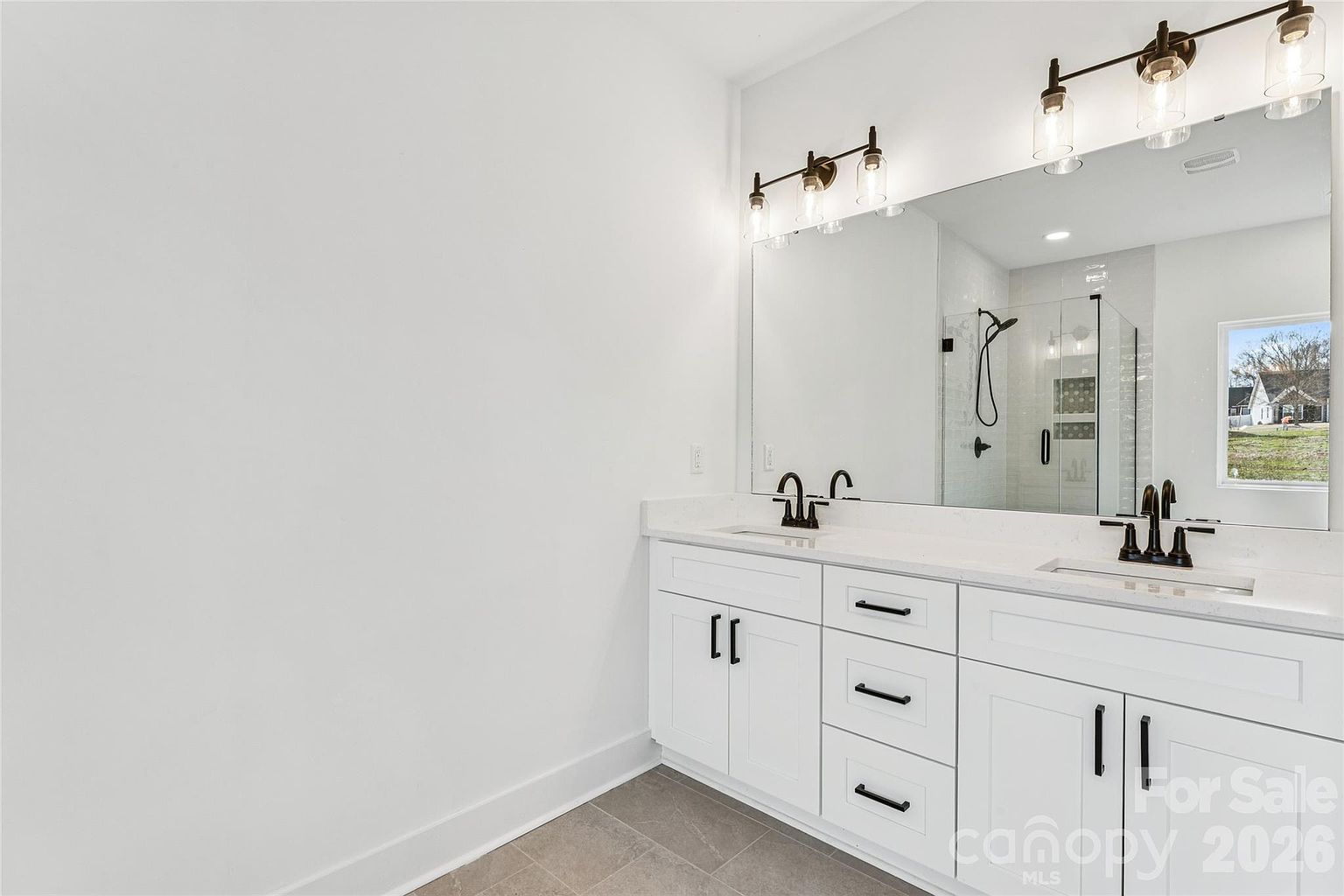Primary bathroom double vanity with quartz countertop, large mirror, oil-rubbed bronze fixtures, and glass-jar sconce lighting