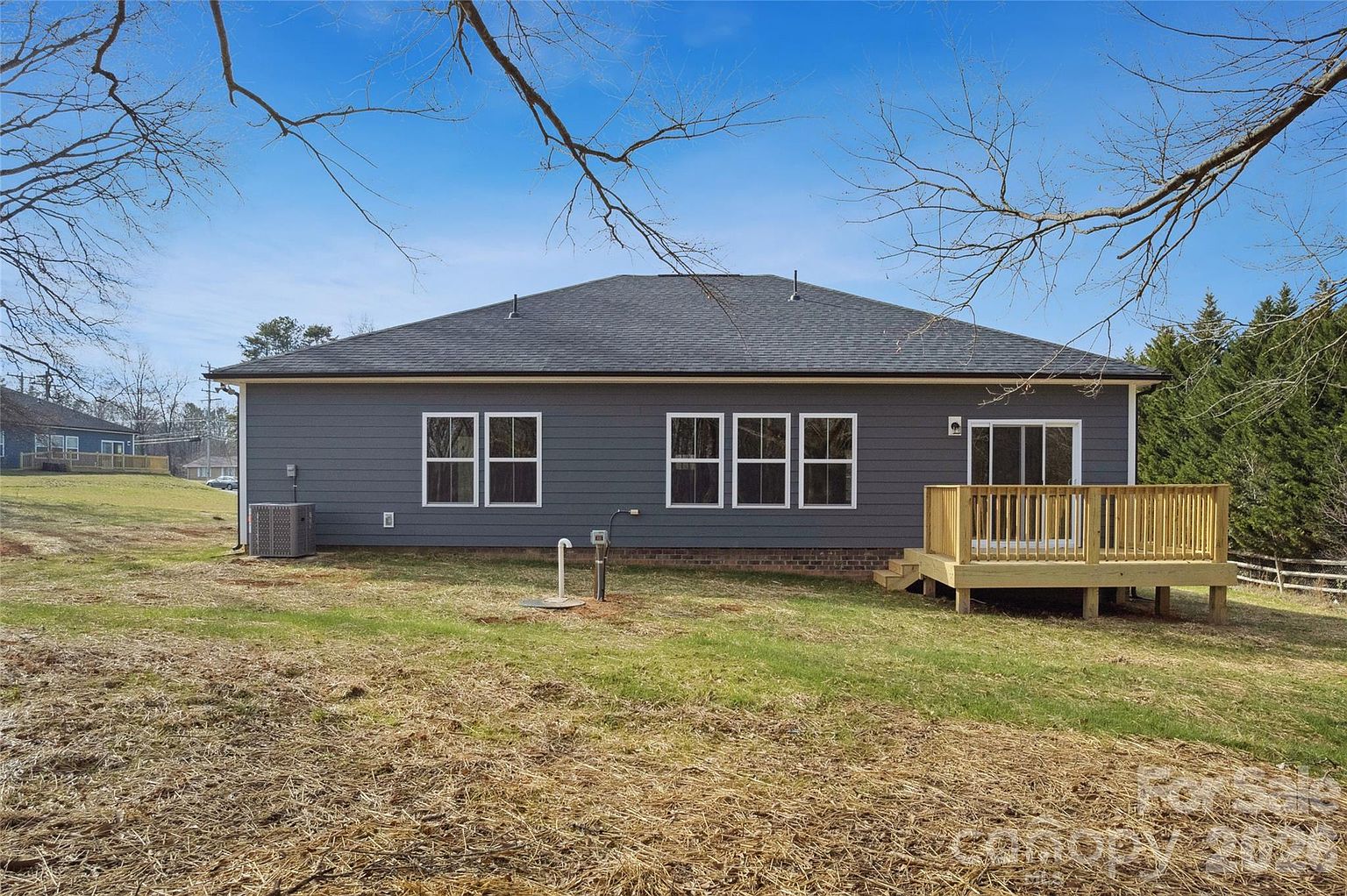 Back of the home from the yard showing the full roofline, rear windows, and deck with steps