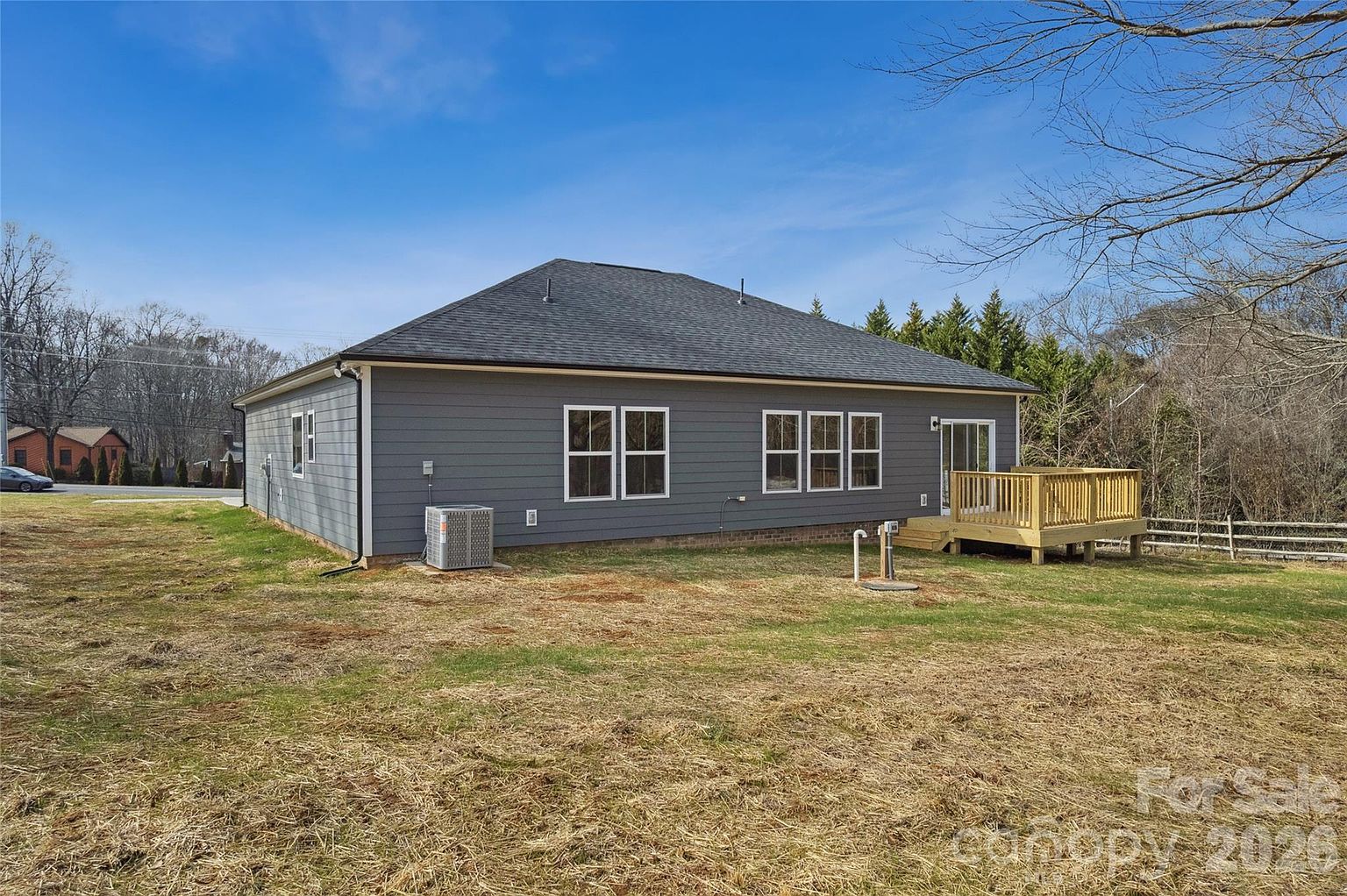 Rear corner view of the home and backyard showing the spacious lot with trees and a neighboring property in the distance