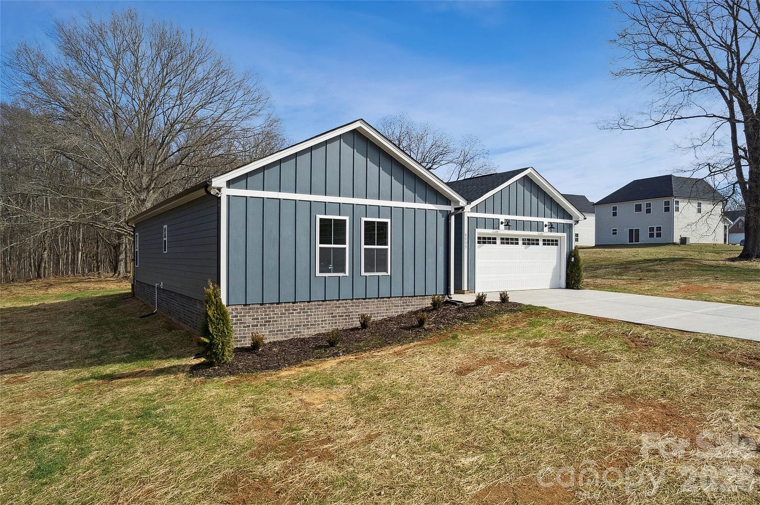 Side view of the home showing blue-gray siding, stone accent base, and a neighboring lot with mature trees