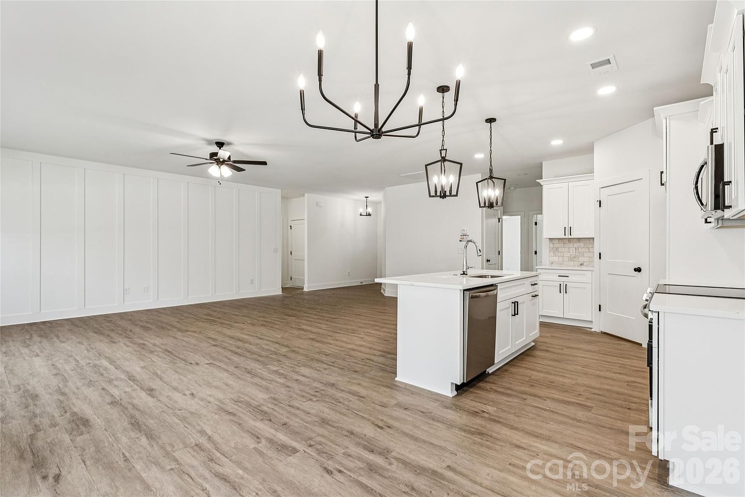Kitchen island with quartz countertop, modern pendant lights, stainless steel dishwasher, and open view to the living area